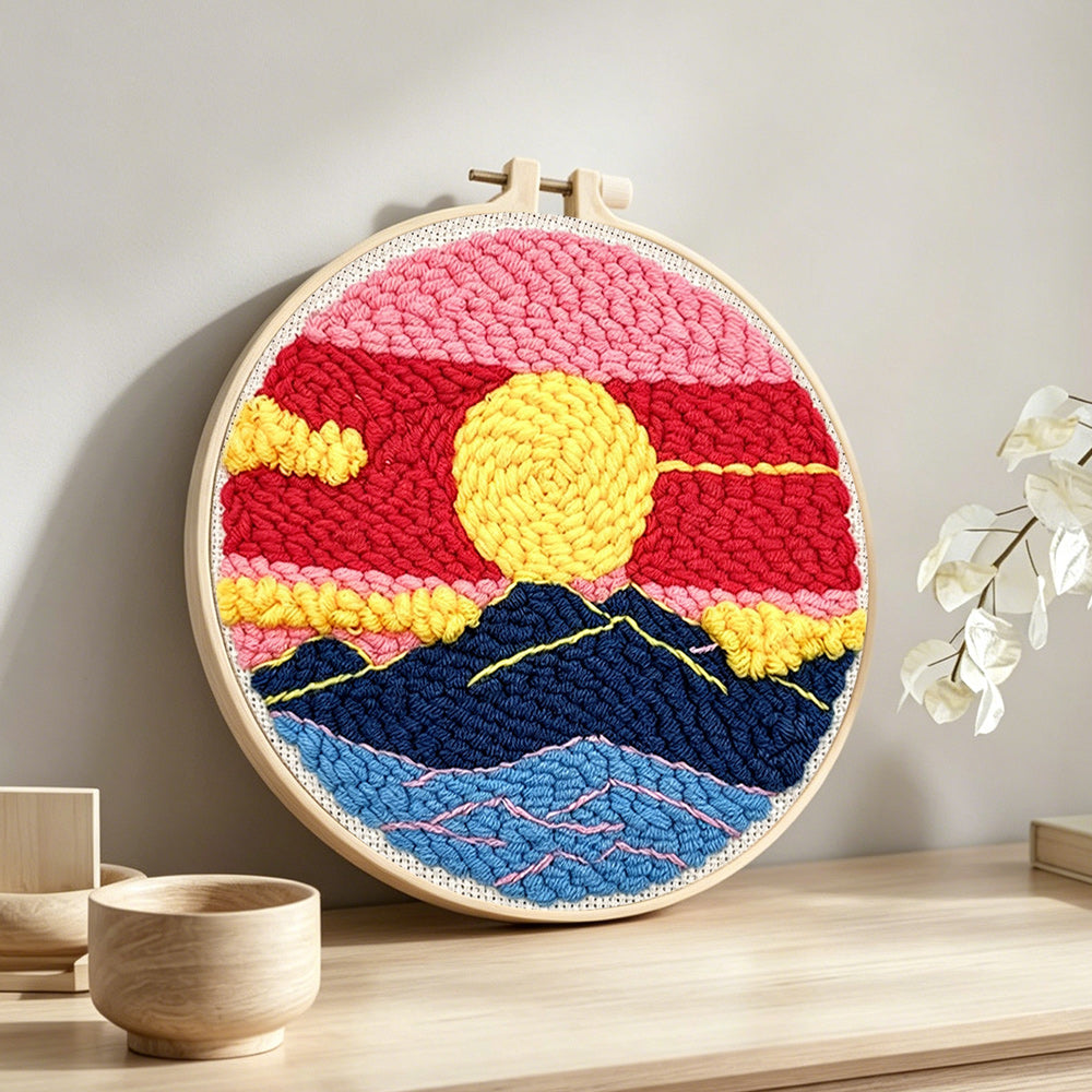 Sun over mountains with pink and red sky punch needle artwork displayed on a table